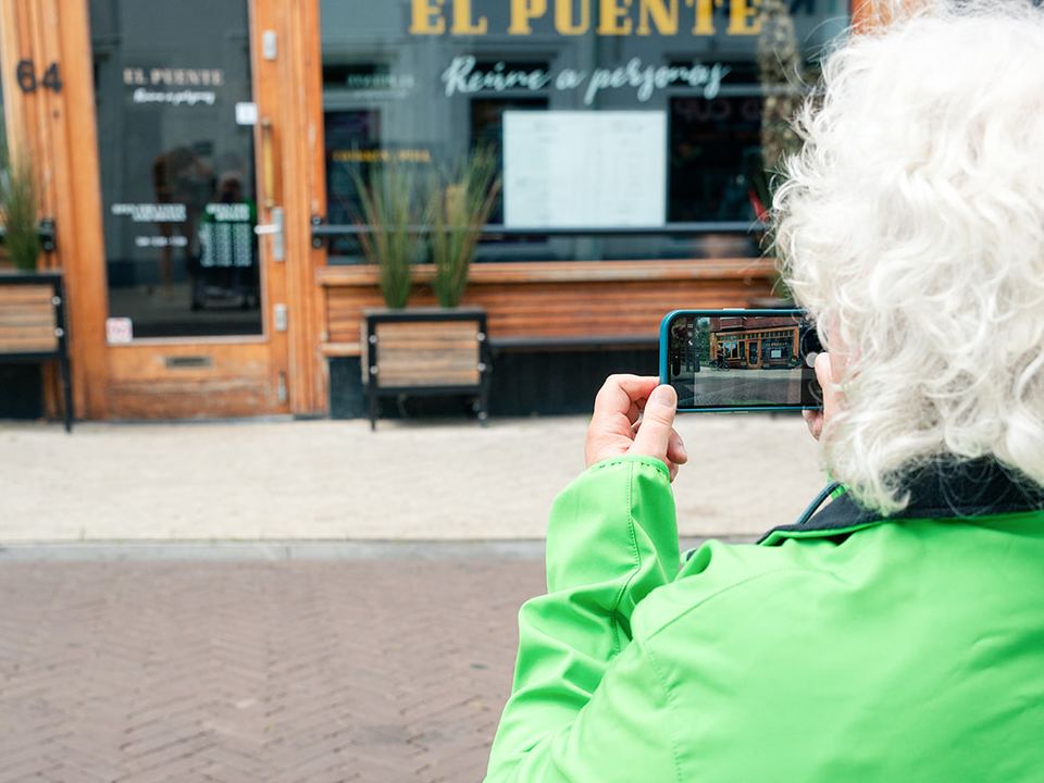 Een ambassadeur van Ongehinderd in een rolstoel fotografeert met haar telefoon de ingang van een restaurant.
